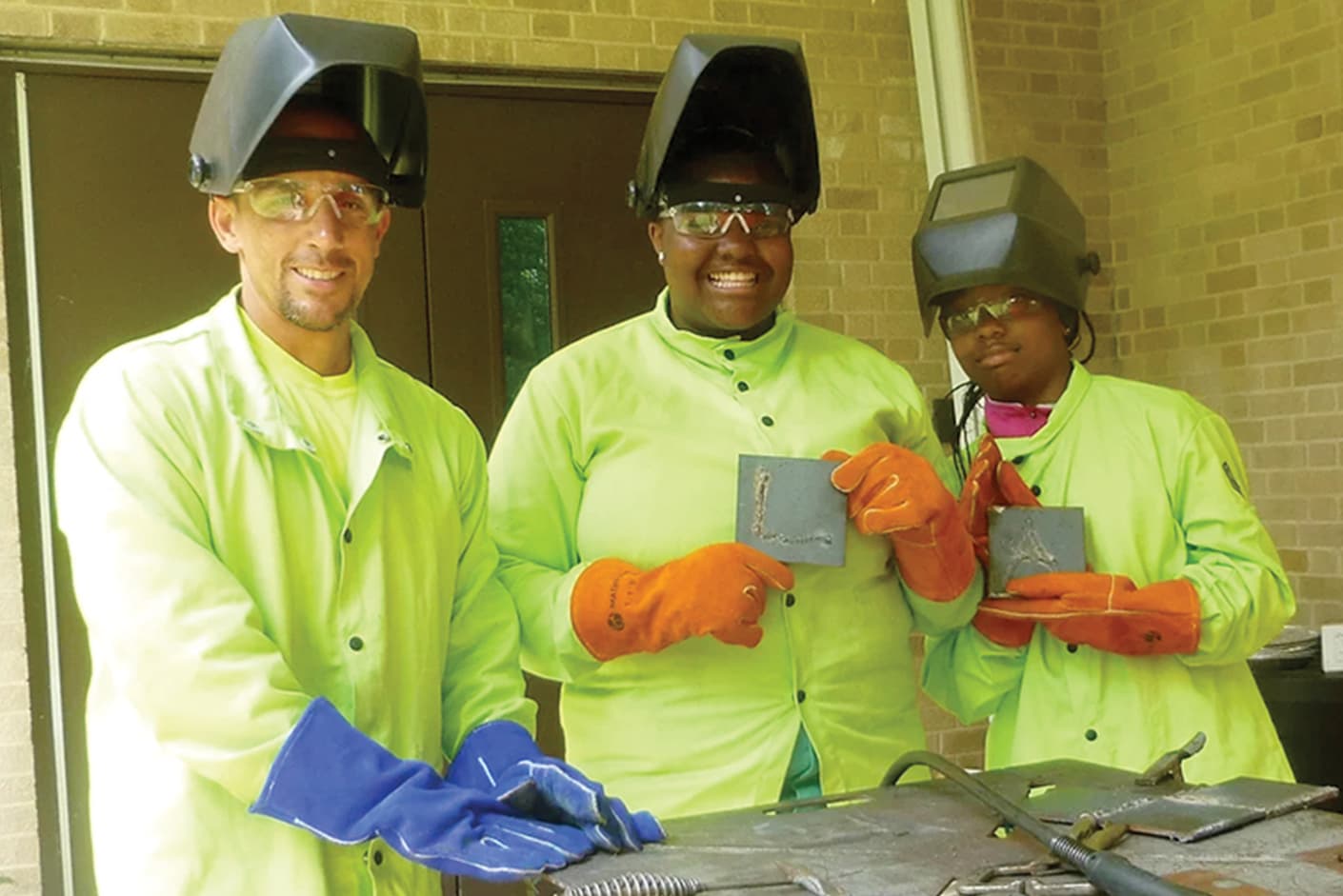 Two kids with a teacher holding up their welding